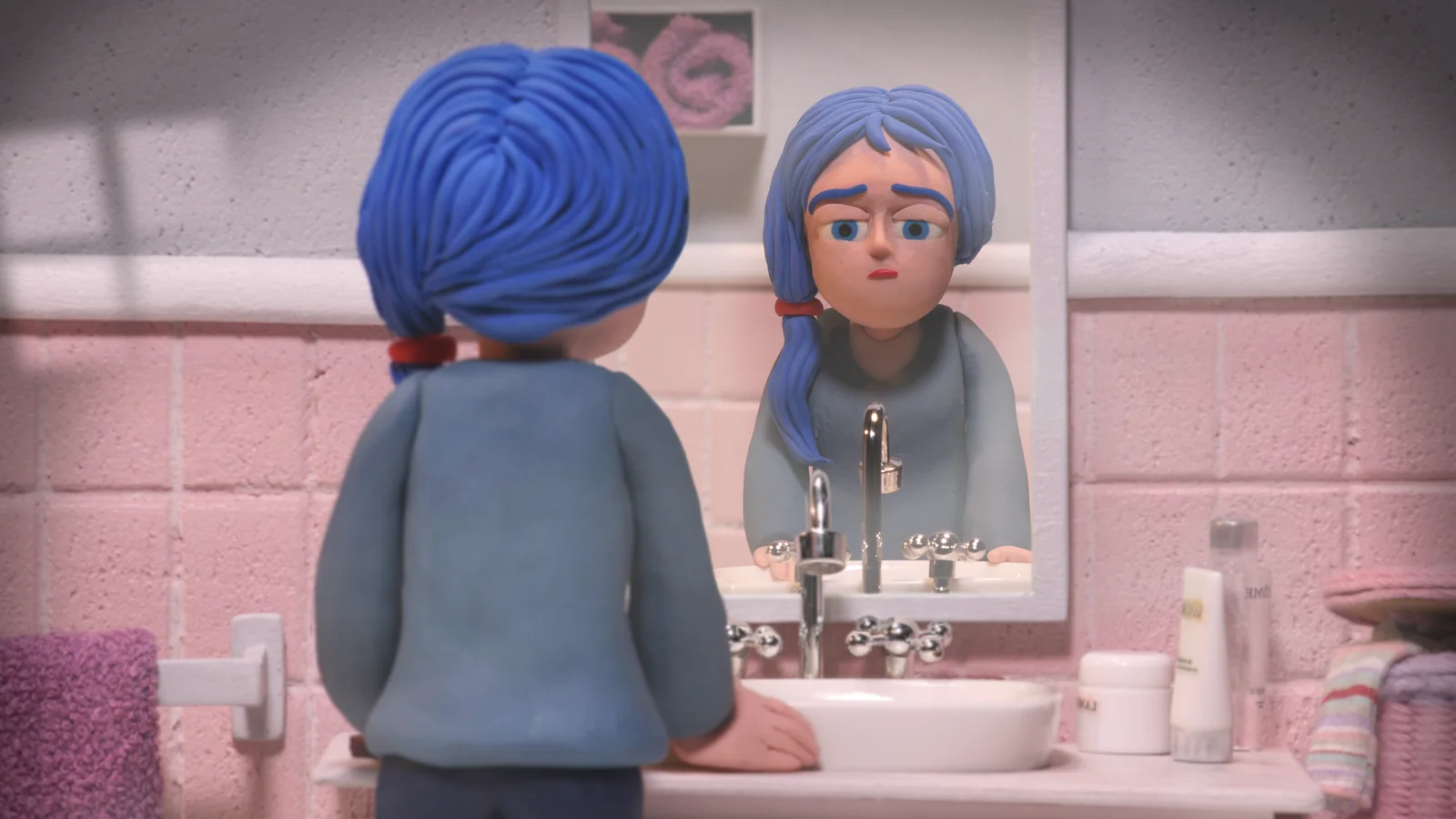 Animación en plastilina de una joven de pelo azul de espaldas, frente a un espejo de baño de azulejos rosas.