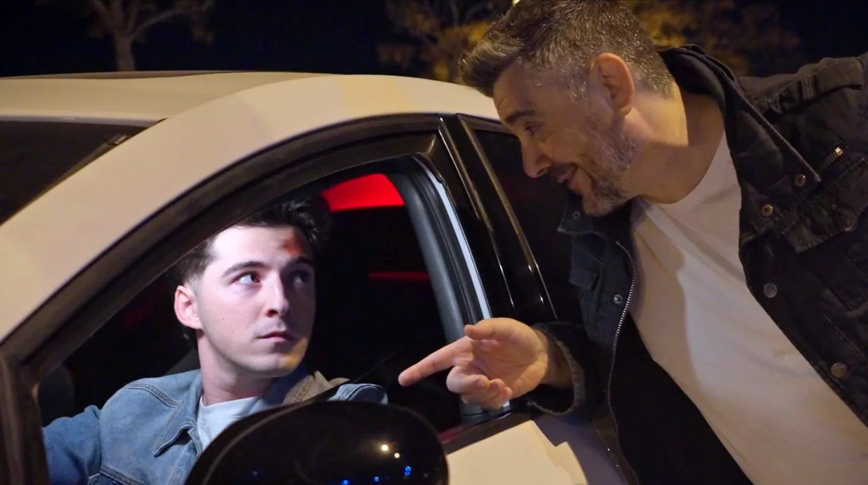 Fotograma de «Feel the gap»: un joven al volante de un coche escucha a un hombre que le habla desde la ventanilla, de noche.