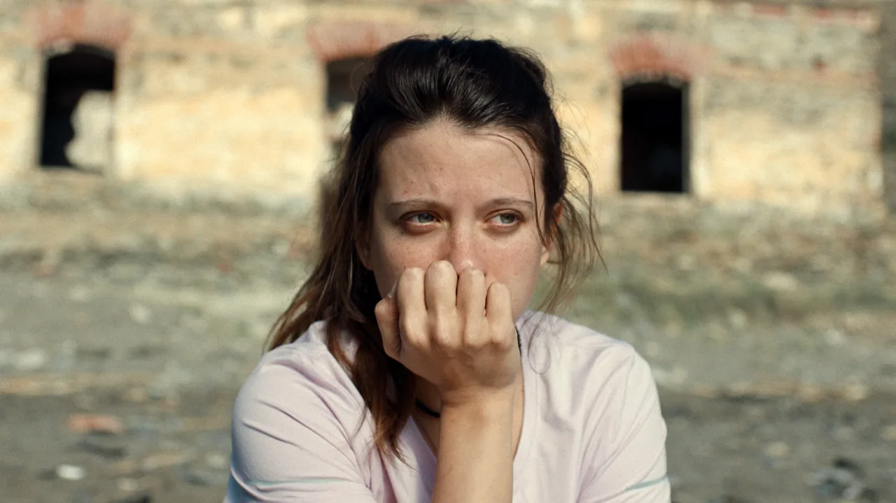 Fotograma de «Fenicia»: una joven pensativa, con la mano en la boca, ante unas ruinas de piedra.