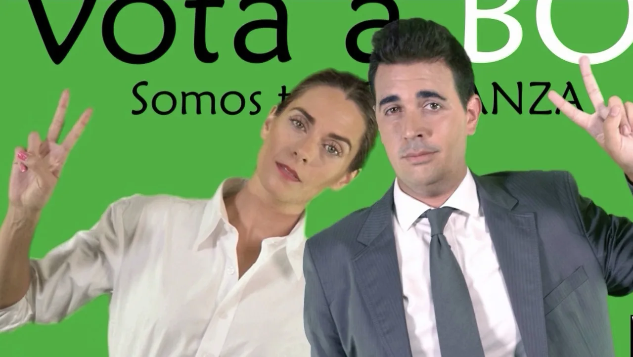 Fotograma de «Importante»: una mujer y un hombre trajeados posan sonrientes ante un cartel electoral verde.