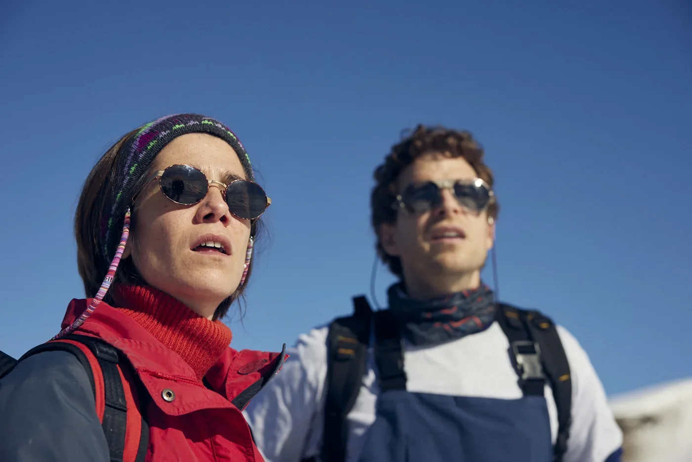 Fotograma de «Balandrau, viento salvaje»: una mujer y un hombre con gafas de sol y ropa de montaña miran hacia arriba bajo un cielo azul.