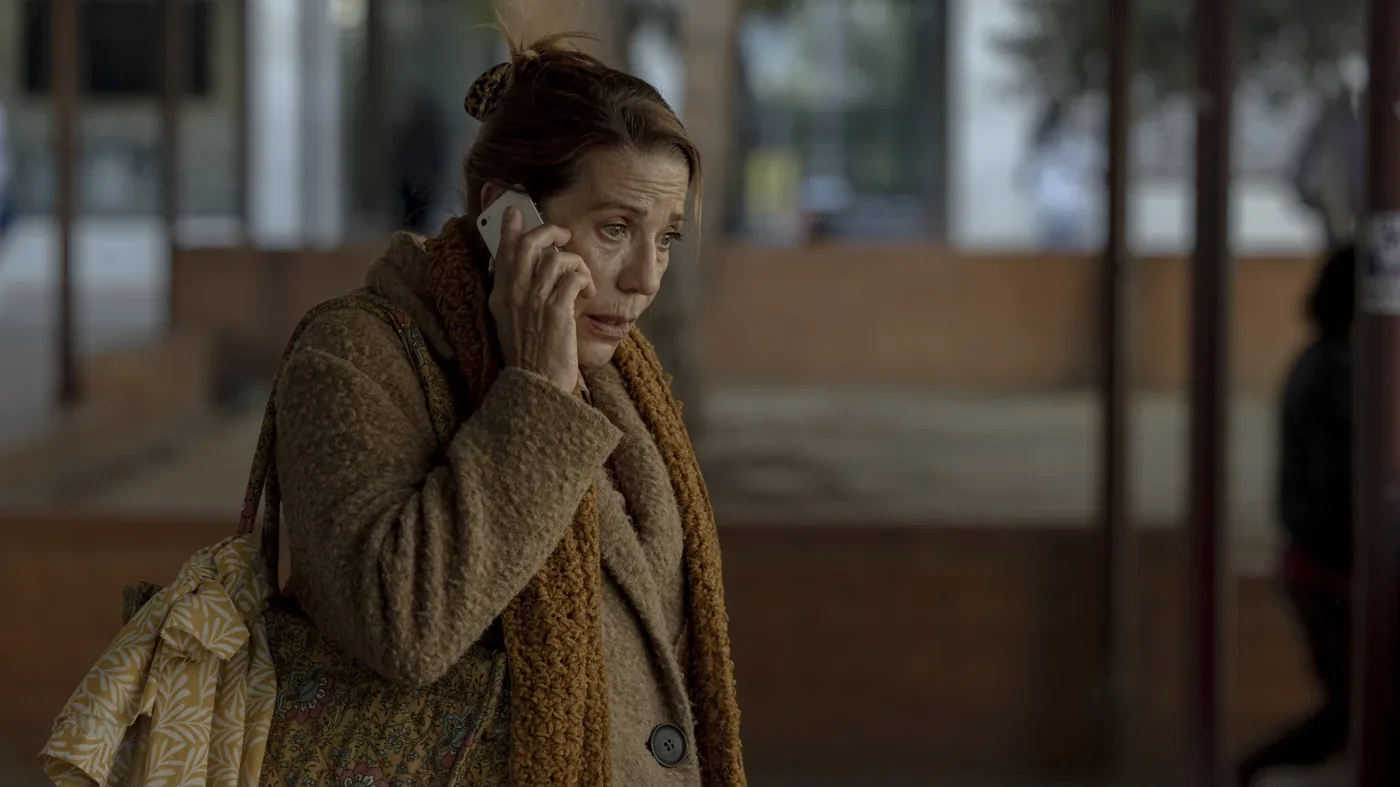 Fotograma de «Viaje al país de los blancos»: una mujer con abrigo habla por teléfono con gesto preocupado.